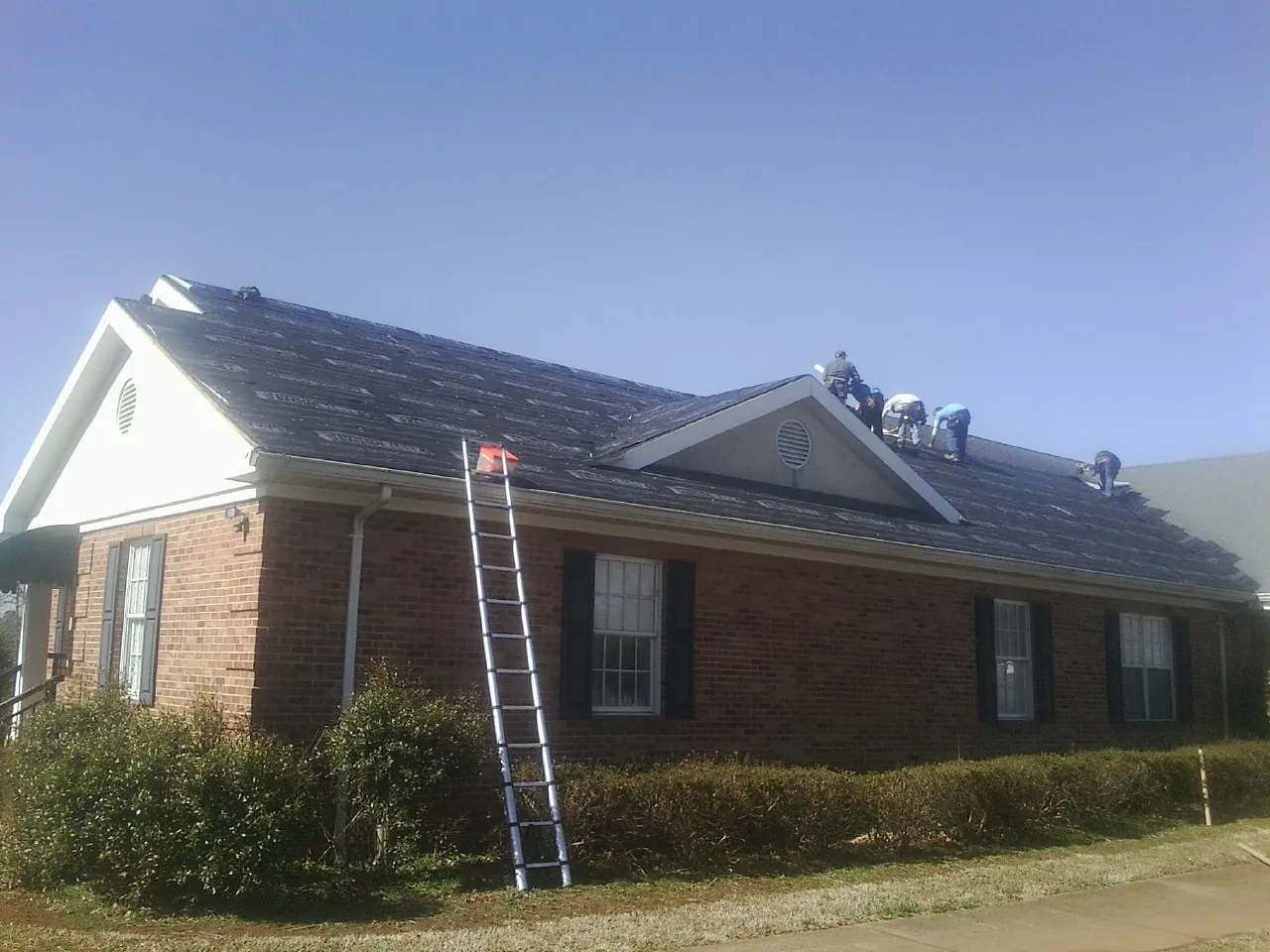 Crew tearing shingles off a brick ranch roof with a ladder set — Metal Roof Repair work by our crew in Mars Hill