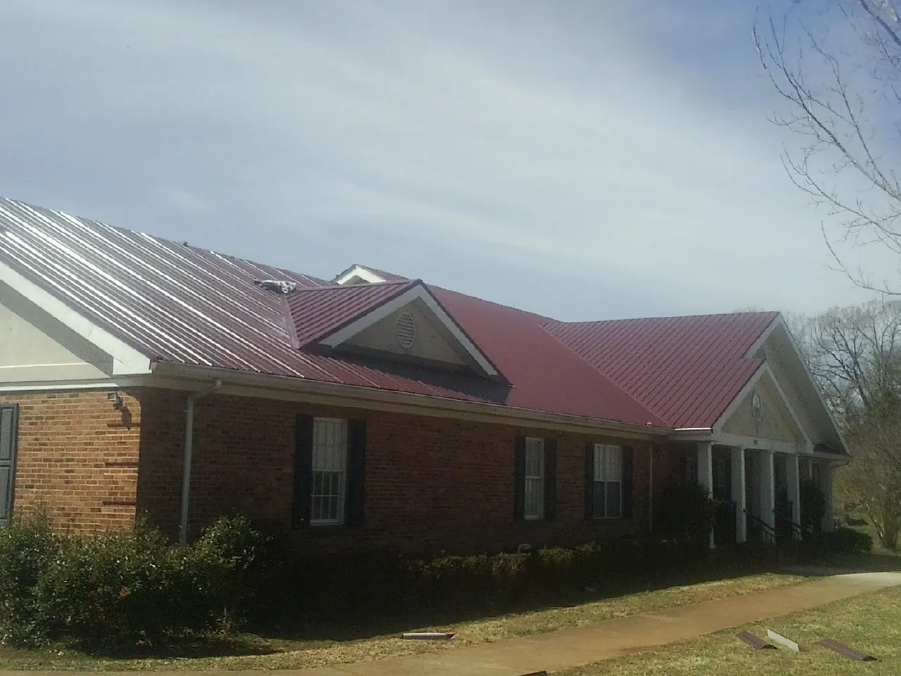Red metal roof with gabled entries on a long brick building, from a Hail Damage Roof Repair job in Mars Hill