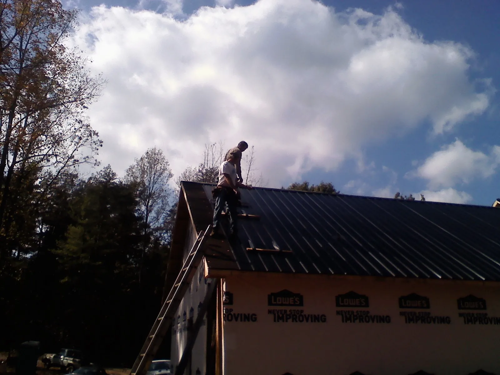 Roofer fastening dark metal panels high against a cloudy sky, from a Roof Inspection job in Mars Hill