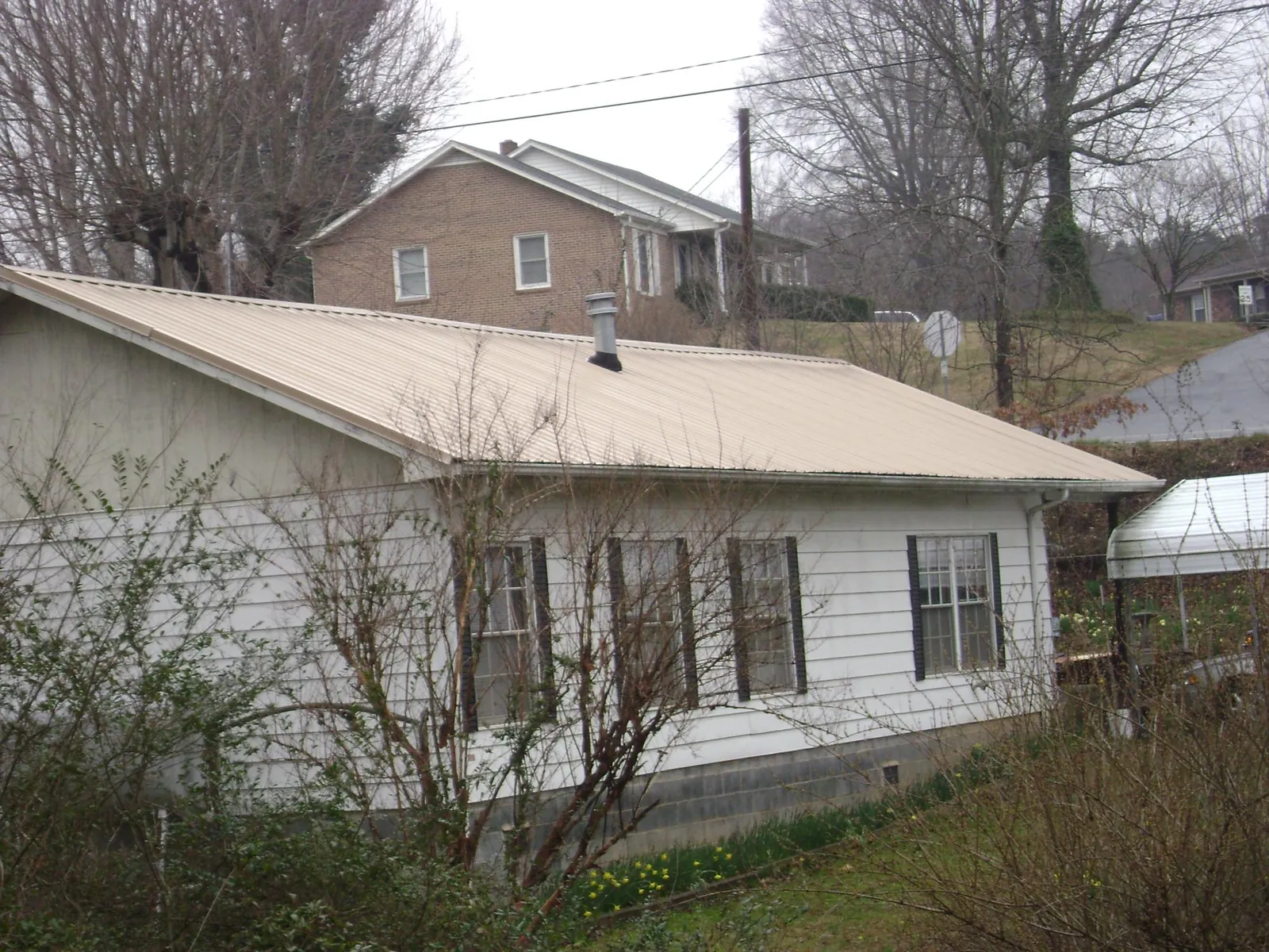 Tan metal roof on a white sided house set into a hillside — Commercial Roofing by Roofing Brothers in Mars Hill