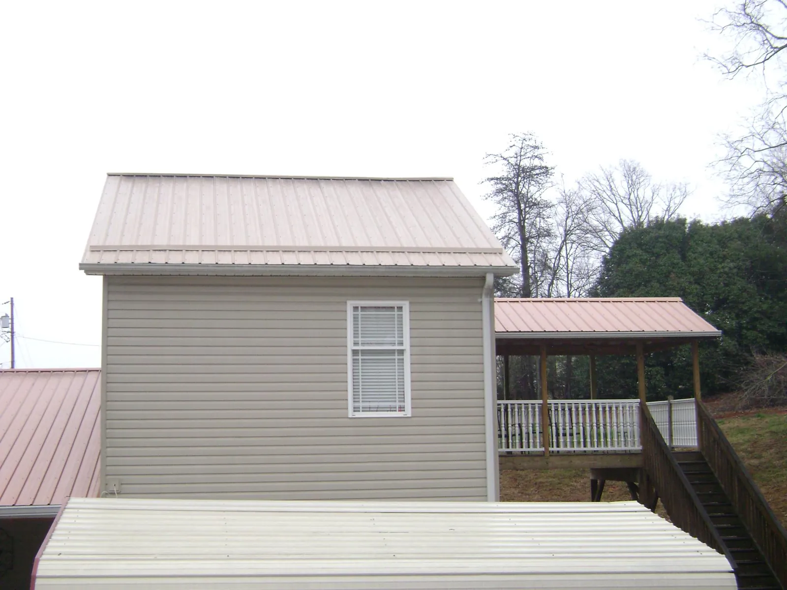Tan metal roofs on a two story addition and attached porch, from a Roof Replacement job in Mars Hill